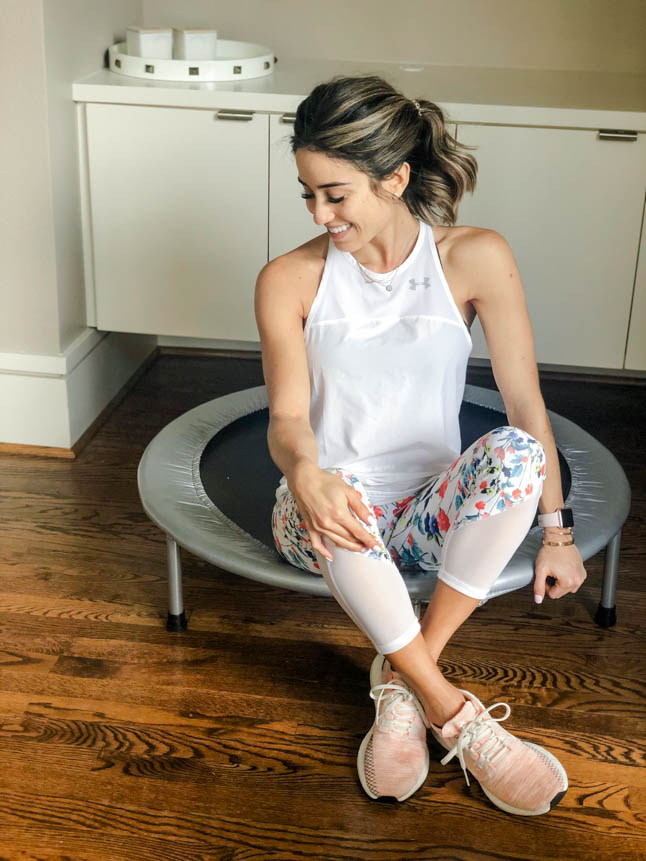 fitness blogger using a small rebounder/mini trampoline in floral printed workout leggings from Fabletics and a white tank sharing a workout at home | adoubledose.com