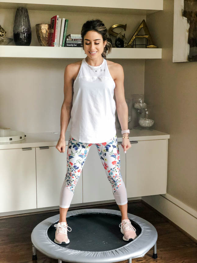 fitness blogger using a small rebounder/mini trampoline in floral printed workout leggings from Fabletics and a white tank sharing a workout at home | adoubledose.com