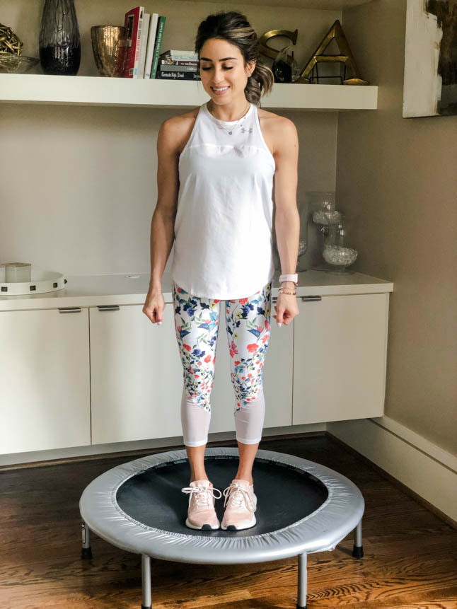 fitness blogger using a small rebounder/mini trampoline in floral printed workout leggings from Fabletics and a white tank sharing a workout at home | adoubledose.com