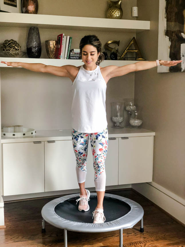 fitness blogger using a small rebounder/mini trampoline in floral printed workout leggings from Fabletics and a white tank sharing a workout at home | adoubledose.com