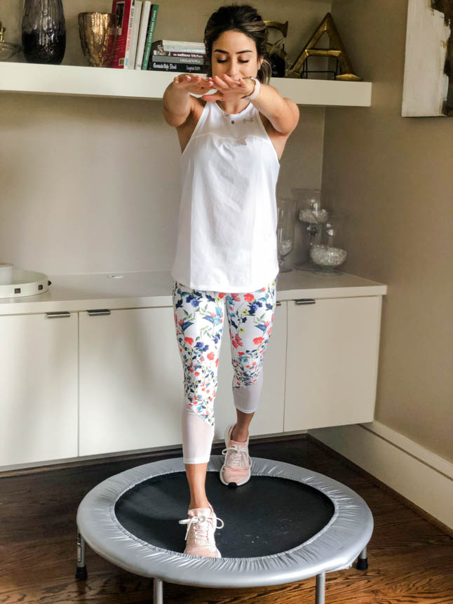 fitness blogger using a small rebounder/mini trampoline in floral printed workout leggings from Fabletics and a white tank sharing a workout at home | adoubledose.com