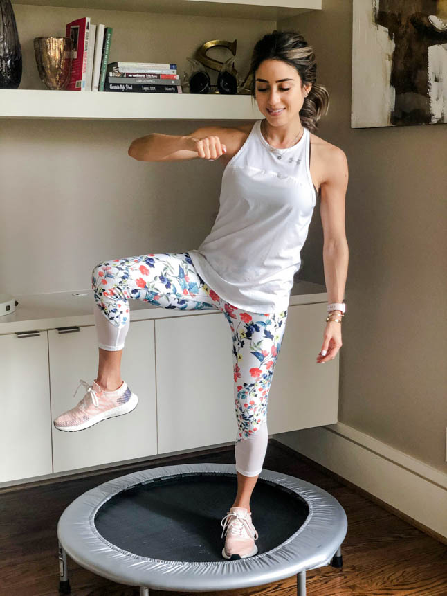 fitness blogger using a small rebounder/mini trampoline in floral printed workout leggings from Fabletics and a white tank sharing a workout at home | adoubledose.com