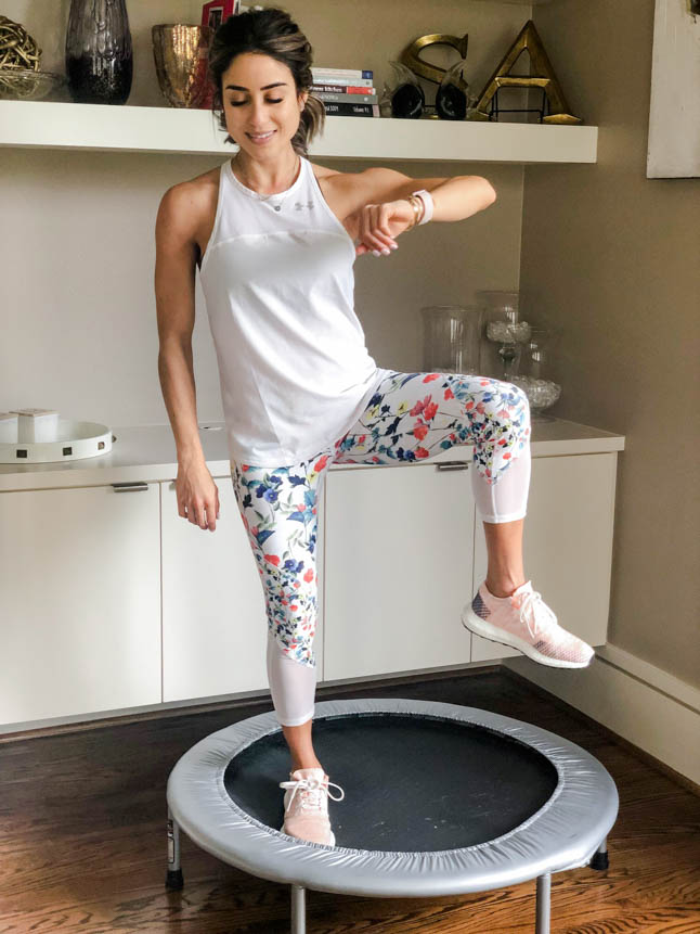 fitness blogger using a small rebounder/mini trampoline in floral printed workout leggings from Fabletics and a white tank sharing a workout at home | adoubledose.com