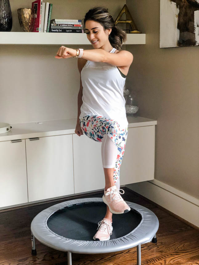fitness blogger using a small rebounder/mini trampoline in floral printed workout leggings from Fabletics and a white tank sharing a workout at home | adoubledose.com