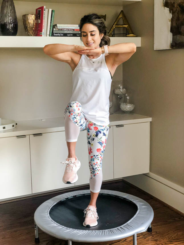 fitness blogger using a small rebounder/mini trampoline in floral printed workout leggings from Fabletics and a white tank sharing a workout at home | adoubledose.com