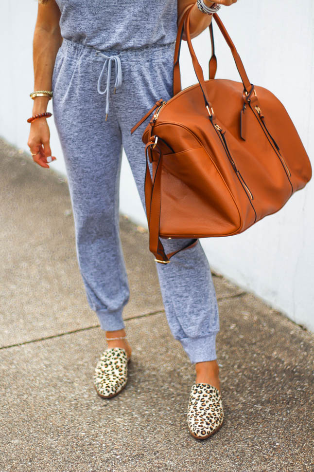fashion blogger wearing grey jumpsuit from express with leopard printed mules from sole society and a cognac weekender travel bag with aviator sunglasses and white lisi lerch earrings