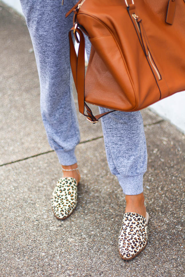 fashion blogger wearing grey jumpsuit from express with leopard printed mules from sole society and a cognac weekender travel bag with aviator sunglasses and white lisi lerch earrings